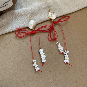 Détail de boucles d'oreilles pompon rouge avec nœud tissé et coquillages sur lin