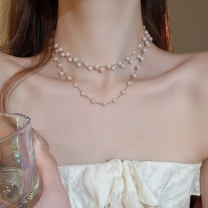 Détail d'un collier de perles superposées avec chaînes dorées sur le cou d'une femme