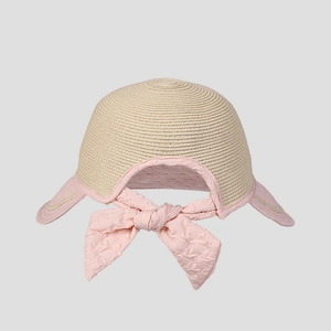 Detail of a kids straw sun hat featuring a pink bow and mesh brim on beige woven texture