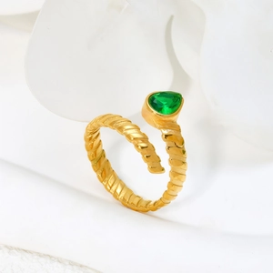 Golden spiral ring with pear-cut green gemstone and textured metal finish on white fabric