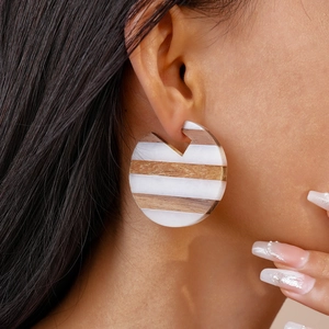 Detail of round wooden and resin striped geometric earring worn on model's ear
