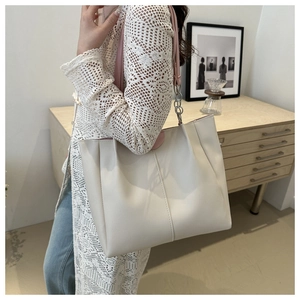 Dettaglio di una borsa tote grande in pelle crema con lati a pieghe e tracolle rosa