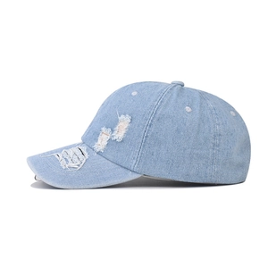 Detail of light blue washed denim baseball cap with vintage distressed holes and silver rings