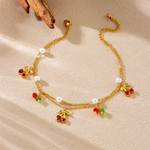 Dual-layer golden anklet with cherry pendants and white pearls on a textured background
