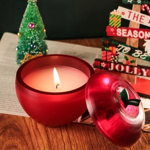 Bougie parfumée en forme de pomme rouge allumée dans un décor festif de Noël