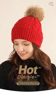 Close-up of red cable knit beanie with fluffy faux fur pom-pom and thick fleece lining
