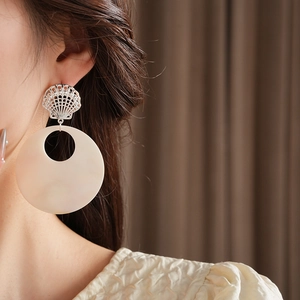 Detail of silver shell stud earring with large cream circular pendant worn by model