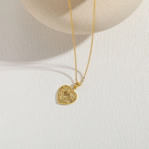 Detailaufnahme eines goldenen Herzanhängers mit Zirkonia auf texturiertem Hintergrund