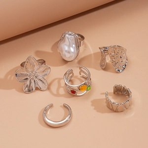 Ensemble de six bagues argentées avec perles et pierres colorées sur fond rose