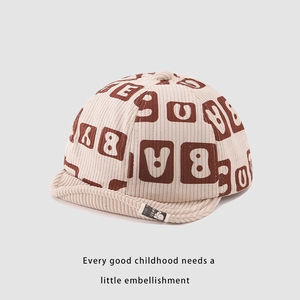 Dettaglio del cappellino neonato in velluto a coste beige con visiera morbida e lettere