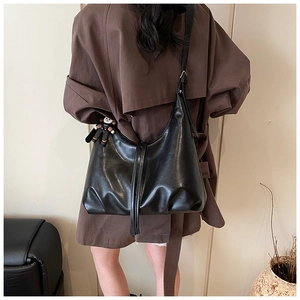 Detail of a black leather hobo bag with adjustable strap and astronaut pendant on shoulder