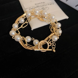 Detail of layered gold snake chain and large link bracelet with pearls and OT buckle