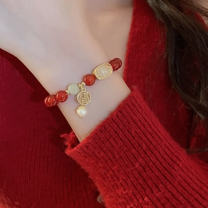Gros plan d'un bracelet en perles rouges avec pendentif Fu doré et jade sur le poignet