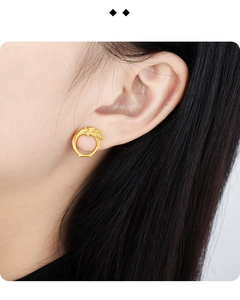 Detailed close-up of matte gold dragon stud earring with zircons on model ear