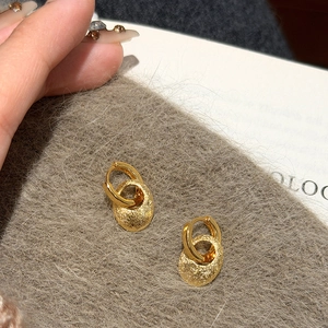 Minimalistische goldene ovale Ohrringe mit gehämmerter Metalloberfläche auf grauem Grund
