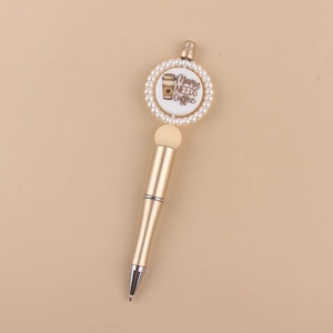 Detailed view of a golden beaded pen with a Mama Needs Coffee printed circular charm