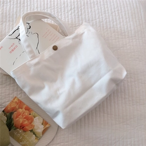 Close-up of a white canvas tote bag showing the bronze magnetic button closure