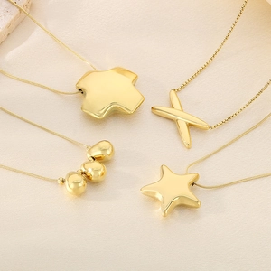 Detail of four gold stainless steel necklaces with star and cross pendants on silk