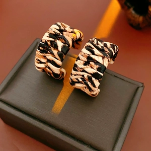 Close-up of woven C-shaped earrings with brown animal print on a black display stand