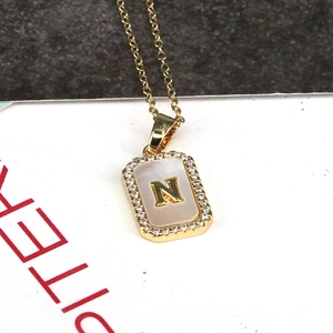 Detail of 18K gold necklace pendant with letter N, white shell, and zircon stones