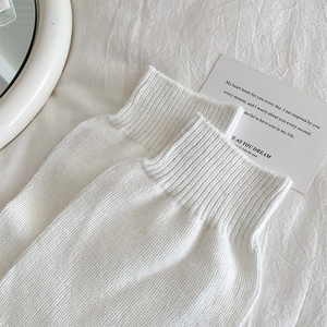 Detail of white knit over-the-knee socks with ribbed cuffs on minimalist bedding
