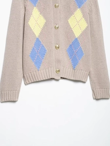 Détail d'un cardigan en maille à losanges avec boutons dorés et texture douce