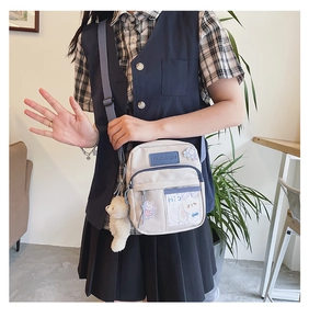 Détail d'un sac bandoulière en toile avec sangles bleues et pendentif ours en peluche