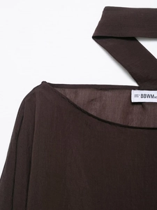 Detail shot of a dark brown woven blouse featuring a round neck and brand care label