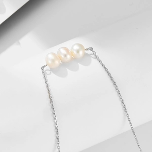 Detailed macro view of three white freshwater pearls on a minimalist silver chain necklace