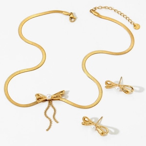 Détail d'un ensemble de bijoux en acier doré avec des nœuds et des perles chic