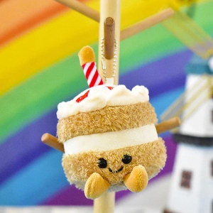 Detail of a cute smiling cupcake plush keychain with a red striped candle