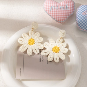 Macro shot of handmade woven raffia daisy earrings with yellow center on white card