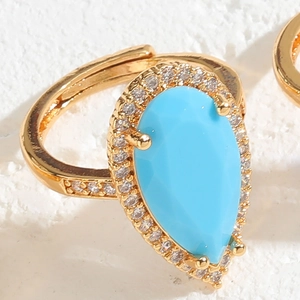 Macro shot of gold ring featuring a pear-cut blue stone with sparkling zircon halo detail