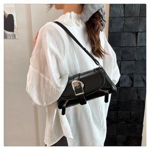 Close-up of black glossy shoulder bag with silver horseshoe buckle on a model