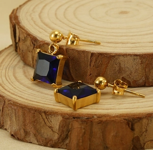 Detail view of 18K gold square blue zircon earrings on a natural wood slice background