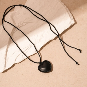 Détail du pendentif cœur en cuir avec bord tressé sur un collier long au style minimaliste
