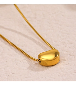 Macro view of gold-plated bean pendant necklace with polished box chain on stone base