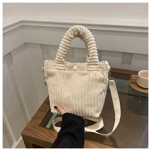 Detail of off-white corduroy bucket bag with snap closure and padded handle design