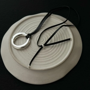 Close-up of polished silver ring pendant with adjustable black cord on ceramic base