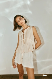 Detail of pleated beige linen sleeveless top with ties and frayed hem cotton shorts