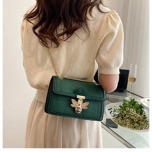 Detail of green snakeskin crossbody bag with vintage gold bee clasp and chain strap