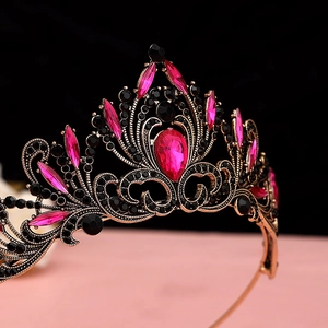 Macro detail of a baroque gold crown featuring pear-shaped magenta gems and black rhinestones