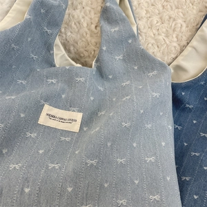 Détail du sac cabas en denim bleu clair avec broderie de nœud blanc sur tapis en peluche