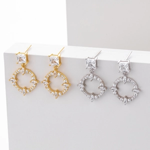 Macro shot of silver and gold geometric drop earrings with cubic zirconia on a white stand
