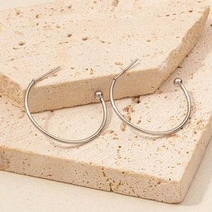 Macro shot of silver C-shape hoop earrings on natural stone showing high-polish texture