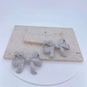 Detail shot of silver bow earrings with sparkling micro-pave crystals on marble stone