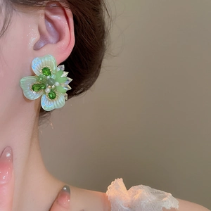 Close-up of a green crystal flower earring with a pearl center on model's ear
