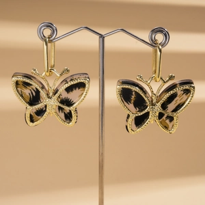 Close-up of golden butterfly drop earrings with leopard print wings on a display stand