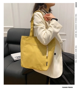 Detail of yellow canvas tote bag featuring front zip pocket and woven tassel charm