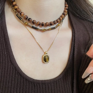 Close-up of layered tiger eye stone necklaces set on a brown textured sweater
